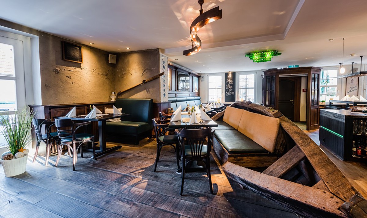 A cozy restaurant interior with wooden flooring, arranged dining tables, and eclectic lighting.