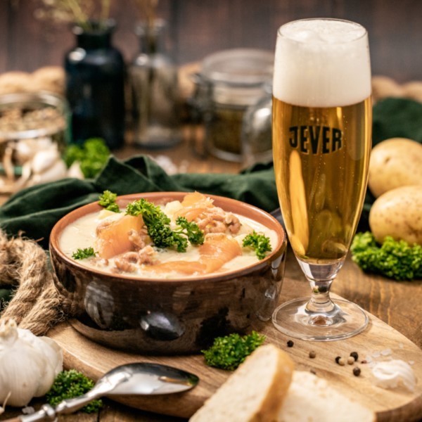 A plate of stew topped with chopped parsley and a glass of light beer are sitting on a wooden table.