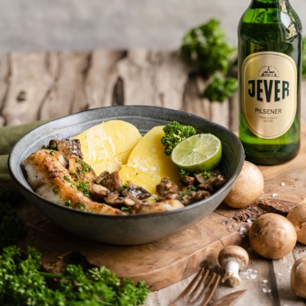 Fried chicken with potatoes and mushrooms is served on a plate. A bottle of beer sits next to it.