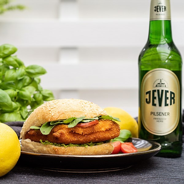 A breaded chicken sandwich with greens on a sesame bun is served beside a bottle of beer – Click for more information about our recipes.