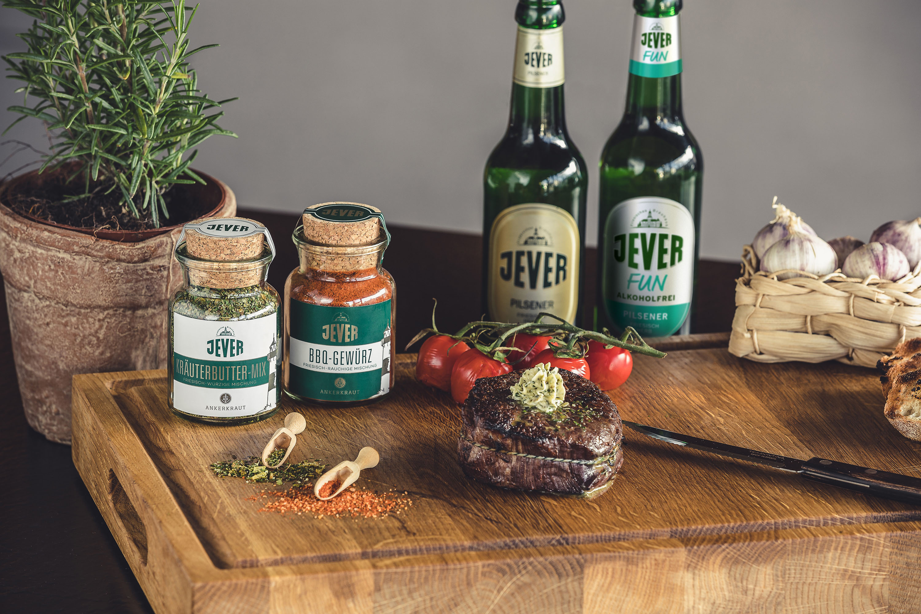 A grilled steak with herb butter on a wooden board, next to spices and beer bottles.